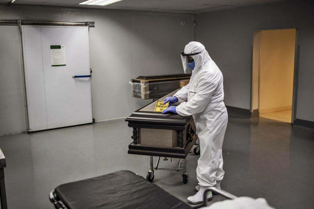 An undertaker wearing personal protective equipment applies a sticker to a casket at the Avbob funeral house in Soweto earlier this week. (Photo: Marco Longari/AFP)